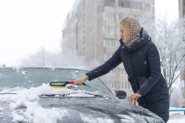 Woman cleaning snow from car windshield, Scraping ice, Winter car window cleaning. Cleaning concept. Winter snow season. Snow covered car.. Cold weather. snow falls.