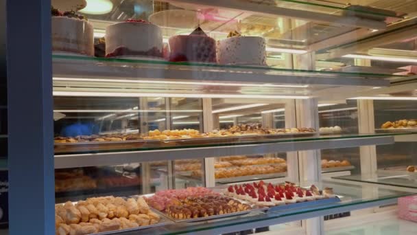 クリーム ケーキまたはベーカリー冷蔵庫のフロスティングが付いているケーキのフルーツ ケーキの変化の選択が付いているガラス ペストリーの店の陳列ケース ベリーと甘いペストリー ショーケース — ストック動画