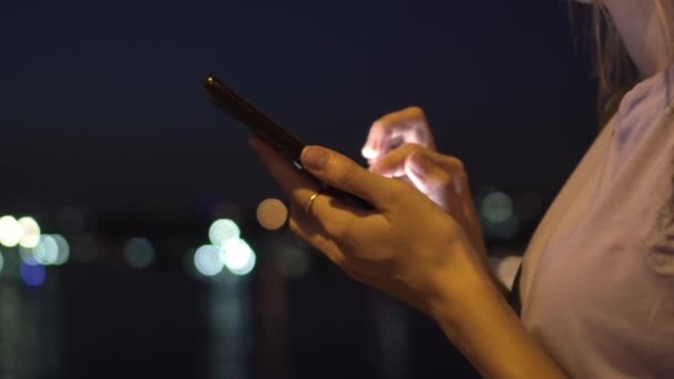 ナイト シティ ストリートに立っている間 マーソンを握っている女性の手の閉鎖 夜の街灯の背景に携帯電話を使用する女性の肖像画 スマートフォン画面を見ている白人ブロンド — ストック動画