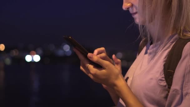 美丽的年轻女子站在夜市大街上看着智能手机 在城市夜灯的背景下使用手机的女人的肖像 白种人金发碧眼看着智能手机屏幕 — 图库视频影像