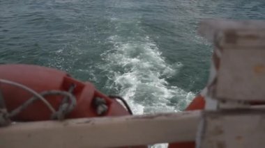 Güverteden ve yandan, denizde seyreden cankurtaran sandalının can simidi boyunca. Gemi derin mavi denizin köpüklü beyaz dalgalarını kesiyor. Beyaz köpüklü hareket eden pervane motoru ile beyaz kabarcık fırladı