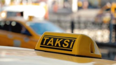 Türkiye 'nin arka planındaki havaalanı terminali veya tren istasyonunun otoparkında bekleyen arabanın çatısındaki sarı taksi sembolünün yakın çekim detayları. Şehir sokak taşımacılığının konforu
