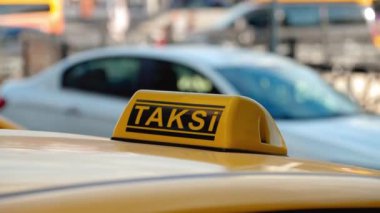 Türkiye 'nin arka planındaki havaalanı terminali veya tren istasyonunun otoparkında bekleyen arabanın çatısındaki sarı taksi sembolünün yakın çekim detayları. Şehir sokak taşımacılığının konforu