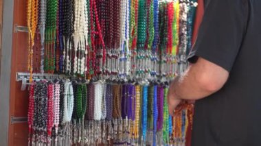 Plastik Tespih Pazarı Genel Bakış, Alıcı El Dokunuşu ve Renkli Plastik Yakın Çekimi. Dini boncuklar ve renkli ipler. Güzel Müslüman tespihi. Dualar için renkli bölümler.