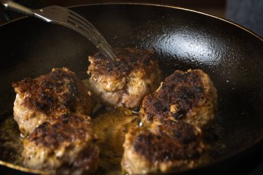 Kızartma tavasında kıymalı pirzola yakın plan. Aşçı tavadaki pirzolaları çatalla çeviriyor. Pirzolaların Rusça veya Lehçe versiyonu - kotlety.