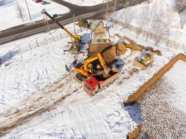 Kazıcının bir kamyona kum döken hava görüntüsü. İnşaat alanının kışın en üst manzarası. Bir İHA 'dan ateş etmek.