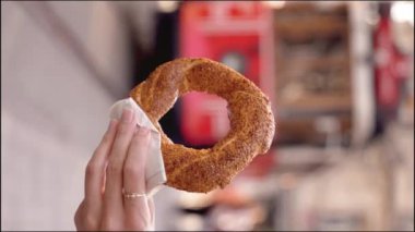Simit 'i, güneşli bir günde, Istiklai şehir caddesinde kırmızı retro garaj yolu ile yakın çekimde tutan turist kız. Susamlı Türk simitleri. Popüler Türk Sokak Gıda Simit. dikey video