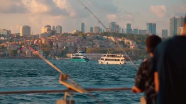 İstanbul 'un arka planında balıkçılık yapan balıkçılar ve gün batımında geçen eğlence tekneleri, Altın Bölgede veya Boğaz' da şehrin güzel panoramik manzarası.