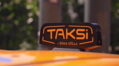 Türkiye 'nin arka planındaki havaalanı terminali veya tren istasyonunun otoparkında bekleyen arabanın çatısındaki sarı taksi sembolünün yakın çekim detayları. Şehir sokak taşımacılığının konforu
