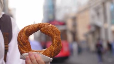 Simit 'i, güneşli bir günde, Istiklai şehir caddesinde kırmızı retro garaj yolu ile yakın çekimde tutan turist kız. Susamlı Türk simitleri. Popüler Türk Sokak Gıda Simit.