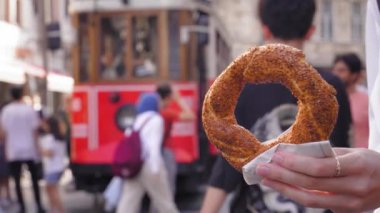 Simit 'i, güneşli bir günde, Istiklai şehir caddesinde kırmızı retro garaj yolu ile yakın çekimde tutan turist kız. Susamlı Türk simitleri. Popüler Türk Sokak Gıda Simit.