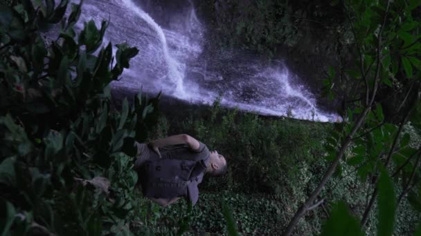 Widok Człowieka Stojącego Przed Wodospadem Facet Plecakiem Stoi Pobliżu Wodospadu — Wideo stockowe