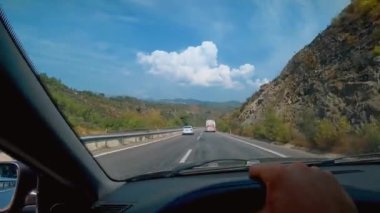 Arabanın ön camından asfalt yoldaki ilk şahıs görüntüsü. Şoförün elleri direksiyonu tutuyor. Yol boyunca doğa, dağlar ve Türkiye 'nin güzel manzaraları.