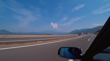 Arabanın ön camından asfalt yoldaki ilk şahıs görüntüsü. Şoförün elleri direksiyonu tutuyor. Yol boyunca doğa, dağlar ve Türkiye 'nin güzel manzaraları.