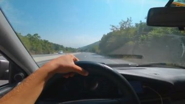 Arabanın ön camından asfalt yoldaki ilk şahıs görüntüsü. Şoförün elleri direksiyonu tutuyor. Yol boyunca doğa, dağlar ve Türkiye 'nin güzel manzaraları.
