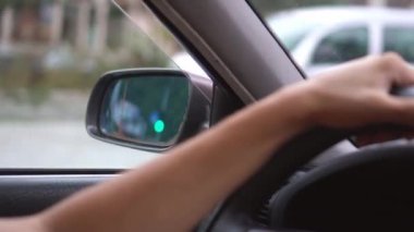 Kabinin içinde araba kullanan adam var. Sürücünün ellerinin direksiyonda yatışı, etraftan geçen çevreye ve manzaraya bakış..