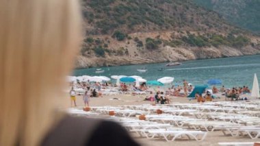 ZMIR, TURKEY - 1 Eylül 2023: Oludeniz plajında güneşlenen ve güneşlenen, güneşli bir günde resimli dağ manzarasına hayran olan bir grup insan.
