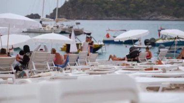 ZMIR, TURKEY - 1 Eylül 2023: Oludeniz plajında güneşlenen ve güneşlenen, güneşli bir günde resimli dağ manzarasına hayran olan bir grup insan.