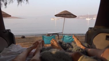 İlk bakışta karavan vagonunda dinlenen kadın ve erkeğin bacaklarını görürüz. Resimli deniz manzarasına karşı. Açık hava yemek alanındayım. Sahilde masa, sandalye ve şemsiye de var..