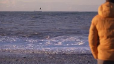 Sarı ceketli bir adamın denizin önünde duruşu. Akşam vaktidir. Sahilin her yerinde altın güneş ışınları parıldıyor. Üzgün ve duygusal bir adam mesafeye bakıyor. Gemi ufukta görünüyor..