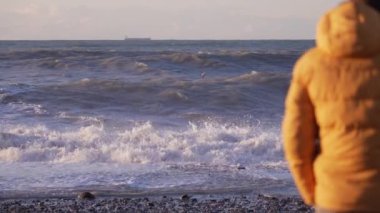 Sarı ceketli bir adamın denizin önünde duruşu. Akşam vaktidir. Sahilin her yerinde altın güneş ışınları parıldıyor. Üzgün ve duygusal bir adam mesafeye bakıyor. Gemi ufukta görünüyor..