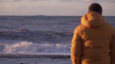Sarı ceketli bir adamın denizin önünde duruşu. Akşam vaktidir. Sahilin her yerinde altın güneş ışınları parıldıyor. Üzgün ve duygusal bir adam mesafeye bakıyor. Gemi ufukta görünüyor..
