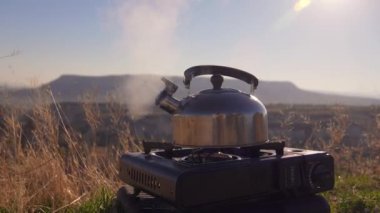 Kamp çaydanlığı gaz kampı sobasının üzerine kurulmuş, dumanlar yükselmeye devam ediyor çarpıcı dağların zemininde. Vahşi doğanın huzurlu güzelliği bu huzurlu kamp sahnesinde yakalanır..