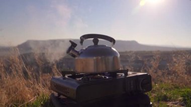 Kamp çaydanlığı gaz kampı sobasının üzerine kurulmuş, dumanlar yükselmeye devam ediyor çarpıcı dağların zemininde. Vahşi doğanın huzurlu güzelliği bu huzurlu kamp sahnesinde yakalanır..