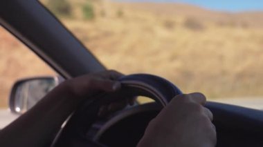 Kabinin içinde araba kullanan adam var. Sürücünün ellerinin direksiyonda yatışı, etraftan geçen çevreye ve manzaraya bakış..