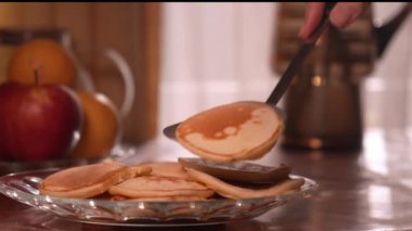 Kadın eli spatula ile tabakta krep, arka planda pencere ve ahşap masada meyve yığıyor. Bir sürü krep yığılmış. Çıtır çıtır krep. Kahvaltı ve karnaval için gözleme..