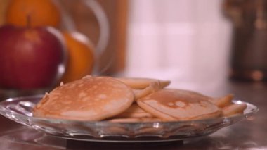 Kadın eli spatula ile tabakta krep, arka planda pencere ve ahşap masada meyve yığıyor. Bir sürü krep yığılmış. Çıtır çıtır krep. Kahvaltı ve karnaval için gözleme..
