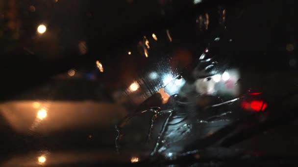 雨滴落在汽车挡风玻璃上 站在夜市街道上的汽车 交通灯的模糊背景 以及开着路灯的汽车 — 图库视频影像