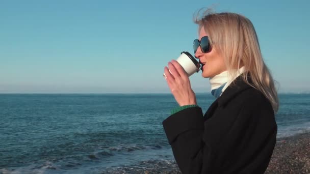 Blondýnka Černém Plášti Slunečních Brýlích Vychutnávající Šálek Kávy Pláži Moře — Stock video