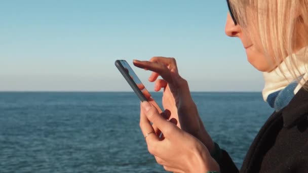 在日出时分 在海滨背景下 年轻女子在户外用手机在线聊天进行特写 人们度假生活方式旅行的概念 — 图库视频影像