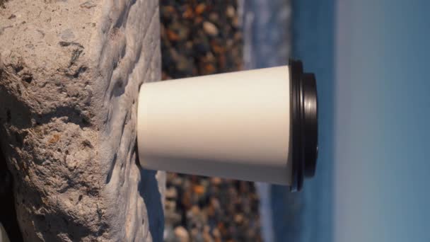 Weiße Papiertasse Mit Kaffee Mit Deckel Bedeckt Auf Kieselstrand Stehend — Stockvideo