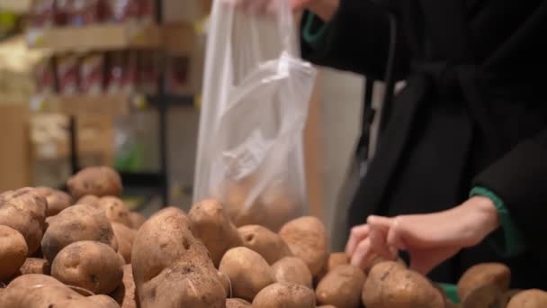 スーパーのカウンターで新鮮なジャガイモを選ぶポテトの女性の買い物客を選ぶ野菜のセクションに手で立っているバッグを持つ若い女性 バッグにジャガイモを入れるクローズアップ — ストック動画