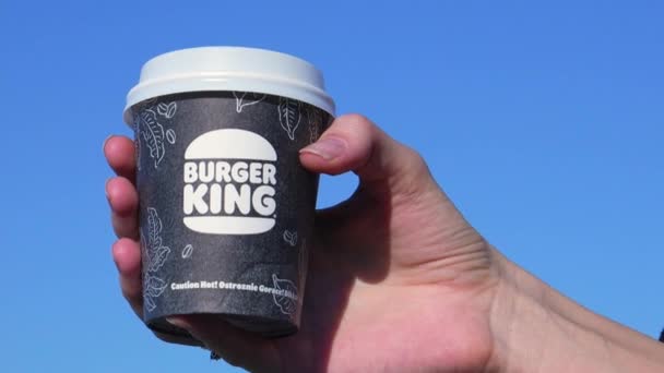 ジョージア州バトゥミ 2024年 バーガーキングのテイクアウトから手札にコーヒーを入れた若い女性 灰色の青い空の背景の女性の手の紙コップのキングコーヒーバーガー — ストック動画