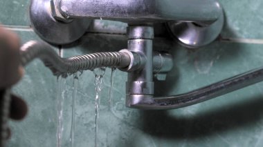 Adamın eli banyoda hasarlı, eski, paslı, sızdıran musluk hortumunu tutuyor. Tesisat sorunu ve musluk tamir gereksinimi kavramı. Tesisatçı