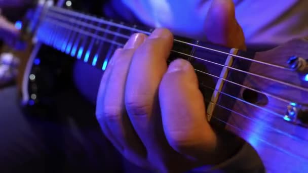 在蓝色灯光下弹奏电吉他 巧妙地弹奏弦乐 在烦躁板上弹奏和弦的音乐家的特写让人着迷 — 图库视频影像