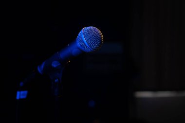 Bir müzik stüdyosunda, karanlıkta bir konserde mavi arka farı olan bir mikrofonun yakın plan görüntüsü.