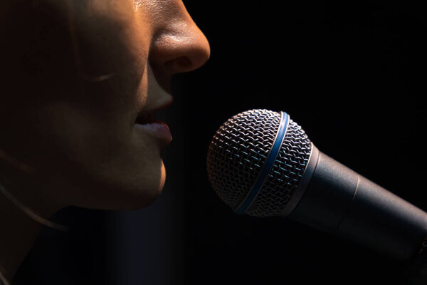 Крупный план микрофона и часть лица молодой певицы на черном фоне