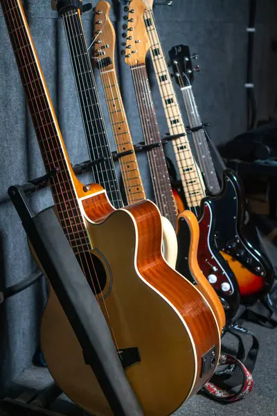 Close-up of beautiful guitars standing in a row near the wall in a music studio or in a store, selective focus. Vertical photo