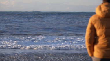 Sarı ceketli bir adamın denizin önünde duruşu. Akşam vaktidir. Sahilin her yerinde altın güneş ışınları parıldıyor. Üzgün ve duygusal bir adam mesafeye bakıyor. Gemi ufukta görünüyor..