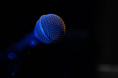 Bir müzik stüdyosunda, karanlıkta bir konserde mavi arka farı olan bir mikrofonun yakın plan görüntüsü.