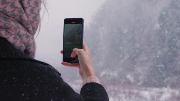 山で写真を撮る若い女性 雪の傘の下の雪の森で携帯電話でビデオ通話をするウィンターウォークガールを楽しんで スローモーション — ストック動画