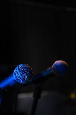 Bir müzik stüdyosunda, karanlıkta bir konserde, arka fonda mavi ışık olan iki mikrofonun yakın çekimi. Seçici odak