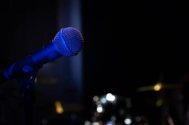 Bir müzik stüdyosunda, karanlıkta bir konserde mavi arka farı olan bir mikrofonun yakın plan görüntüsü.
