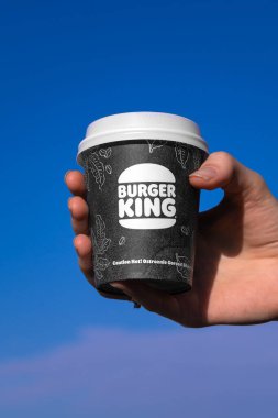 Batumi, Gürcistan - Şubat 12024: Mavi gökyüzü arka planına karşı Burger King kahvesi tutan bir kadının yakın çekimi. Dikey fotoğraf