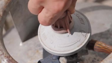 Gaz tüpü yakın plan. Gümüş dağıtıcı gaz silindir vanasına bağlanır ve erkek operatörün eli gaz tüpü doldurma vanasını açmak veya kapatmak için döner.