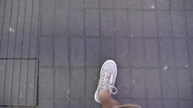 Kotlu ve beyaz spor ayakkabılı bir adam kaldırım levhalarında yürüyor. Birinci şahıs bakış açısıyla insan yürüme ya da sokakta şort ve spor ayakkabılarla gezinme görüntüsü